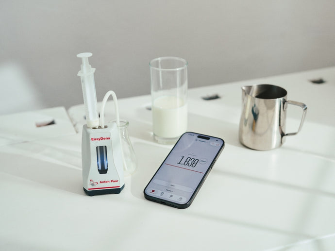 EasyDens on a white table next to a Smartphone with the Lab Meister App Screen and a glass with milk and a small milk creamer made out of steel